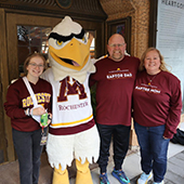 Raptor mascot posing with a student and her parents