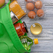 A grocery bag with eggs, oil, pasta sauce and other items spilling out