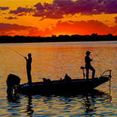 Two people fishing from boat at sunset