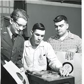 1950s black and white photo of 3 students looking at tape player