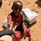 child in somalia sitting on bags of grain