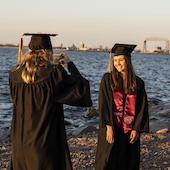 Two women taking photos in caps and gowns along Lake Superior