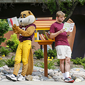 Goldy and student reading in front of Little Free Library