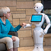 An elderly woman interacts with a small robot