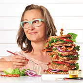 Betsy Nelson sits behind a comically large sandwich