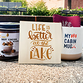 A card, hot cocoa powder, and a coffee mug for sale on a table as part of MN Alumni Market