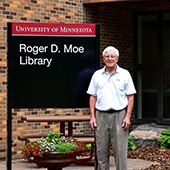 Roger Moe in front of a sign reading Roger Moe Library