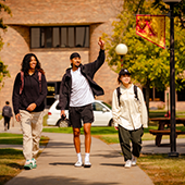three students walk across campus while one waves