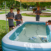 young boys gather around an inflatable pool to test electric floating devices