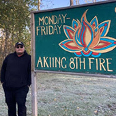 a man stands by a sign reading Akiinc 8th fire 