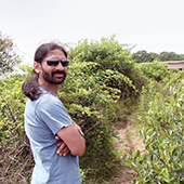 Jacob Haqq Misra standing in a field of bushes