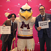 A parent and student take a photo with a raptor mascot 