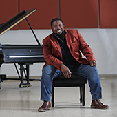 Adrian Davis seated at a piano bench in front of a grand piano