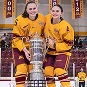 Audrey and Madeline Wethington in hockey gear pose on ice with trophy