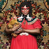 Myah Walker in a bright red dress holding a chicken with a decorative rug background 