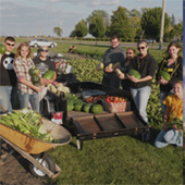 Community members, a dozen or so, show off a recent harvest of produce at the community garden 