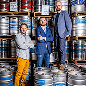 Rob Fisk, David O'Neill, and Jason Dayton stand on kegs in a warehouse