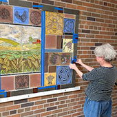 Susan Warner hanging tile art on a brick interior wall