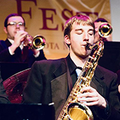 A student plays saxophone with two trumpet players in background
