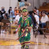 a young boy in traditional Native powwow attire dancing on a gym floor