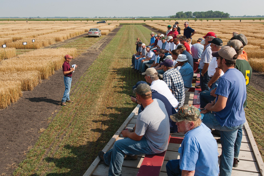 A University of Minnesota employee presents to a large group on bleachers in a farm field.