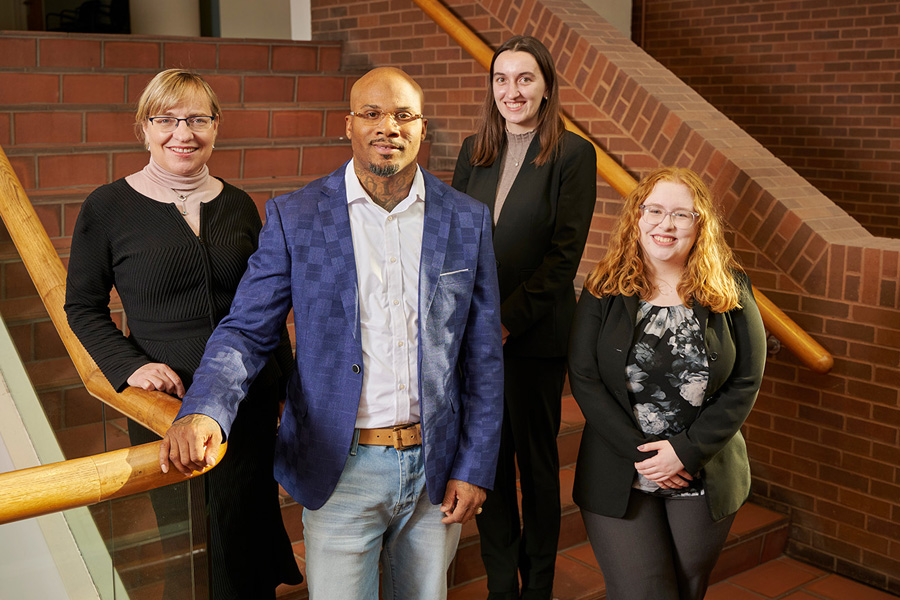 Three women and one man pose for a group photo in a stairwell.