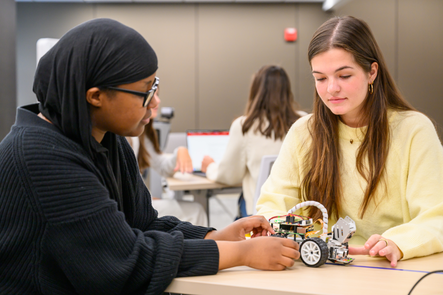 Two female students handle a robot.