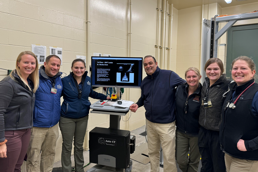 Seven people stand smiling around a computer monitor displaying a medical scan that won an award.
