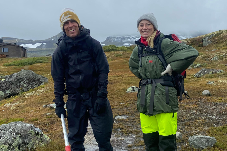 Two people standing in a field with mountains in background.
