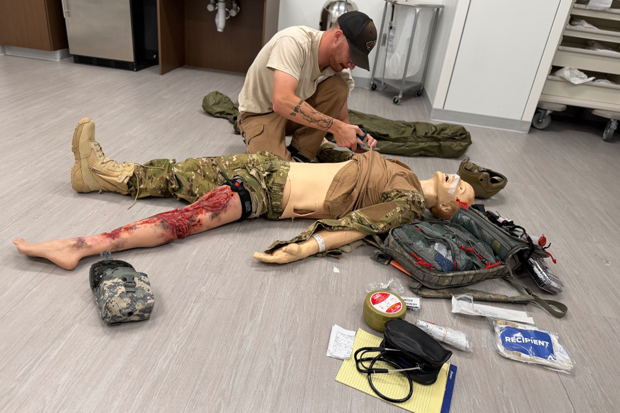 Student performs care on dummy dressed in military attire with a bloody wound.