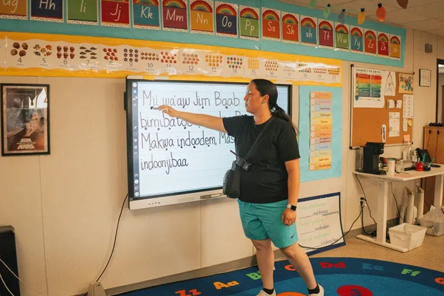A woman writes on a technology board in a classroom.