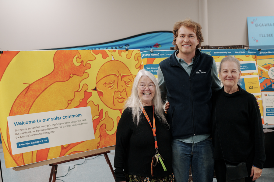 Three people smile at the camera in front of poster boards with orange, yellow and blue art.